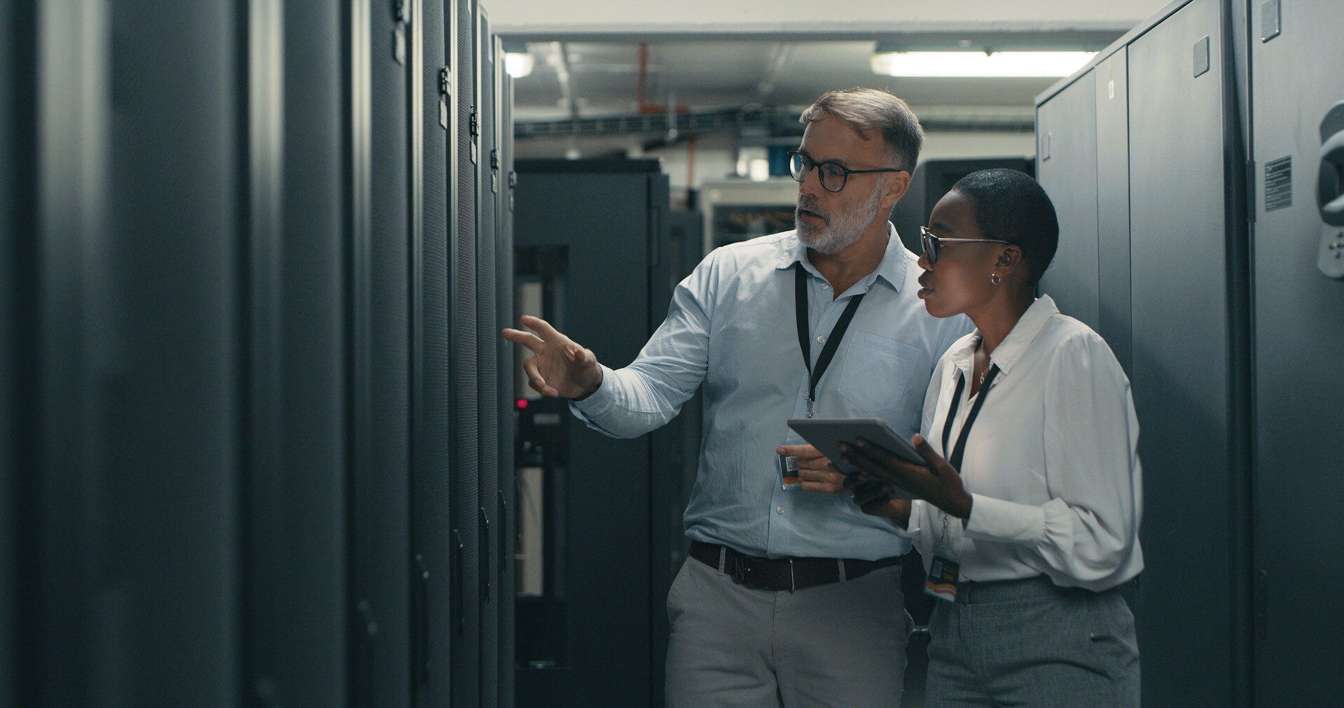 Two People standing in a centre in a data centre looking at a laptop and smiling.